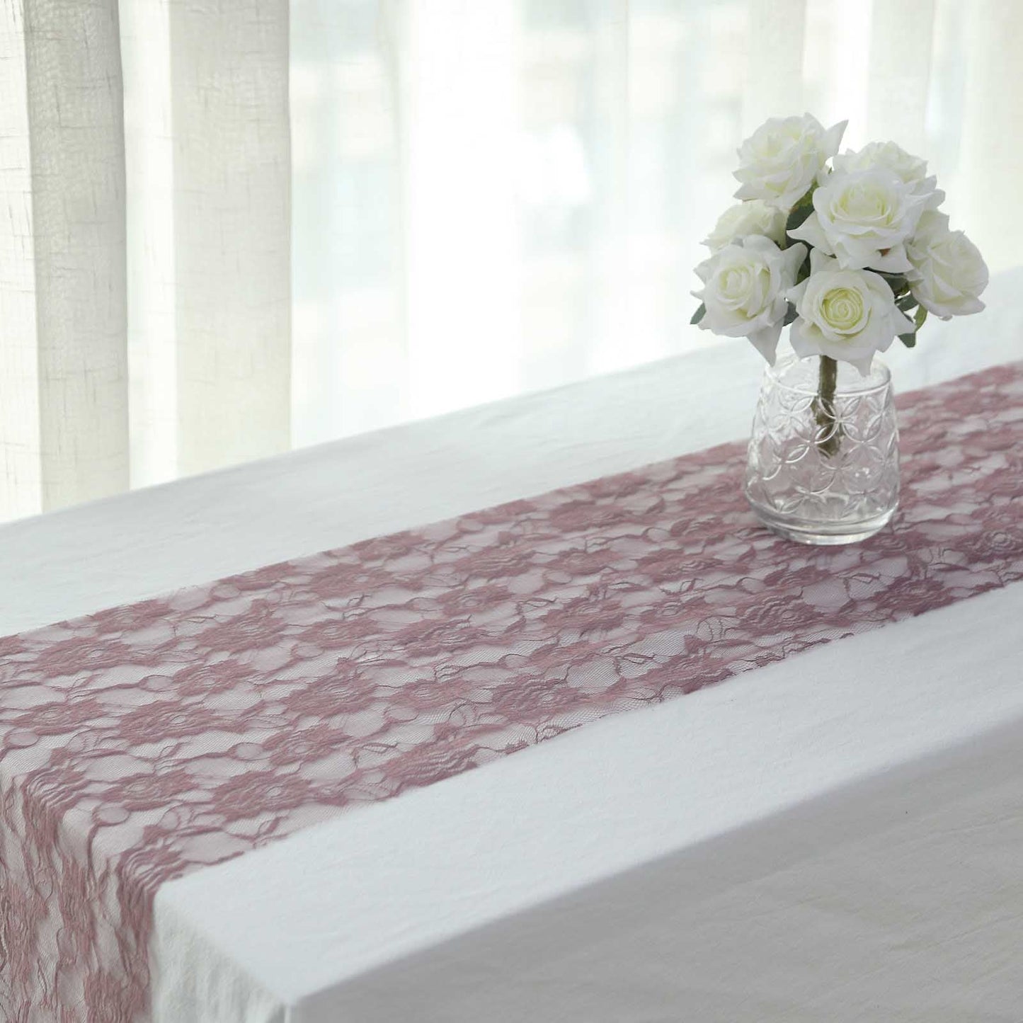 Violet amethyst floral lace table runner on a white table with a vase of roses.