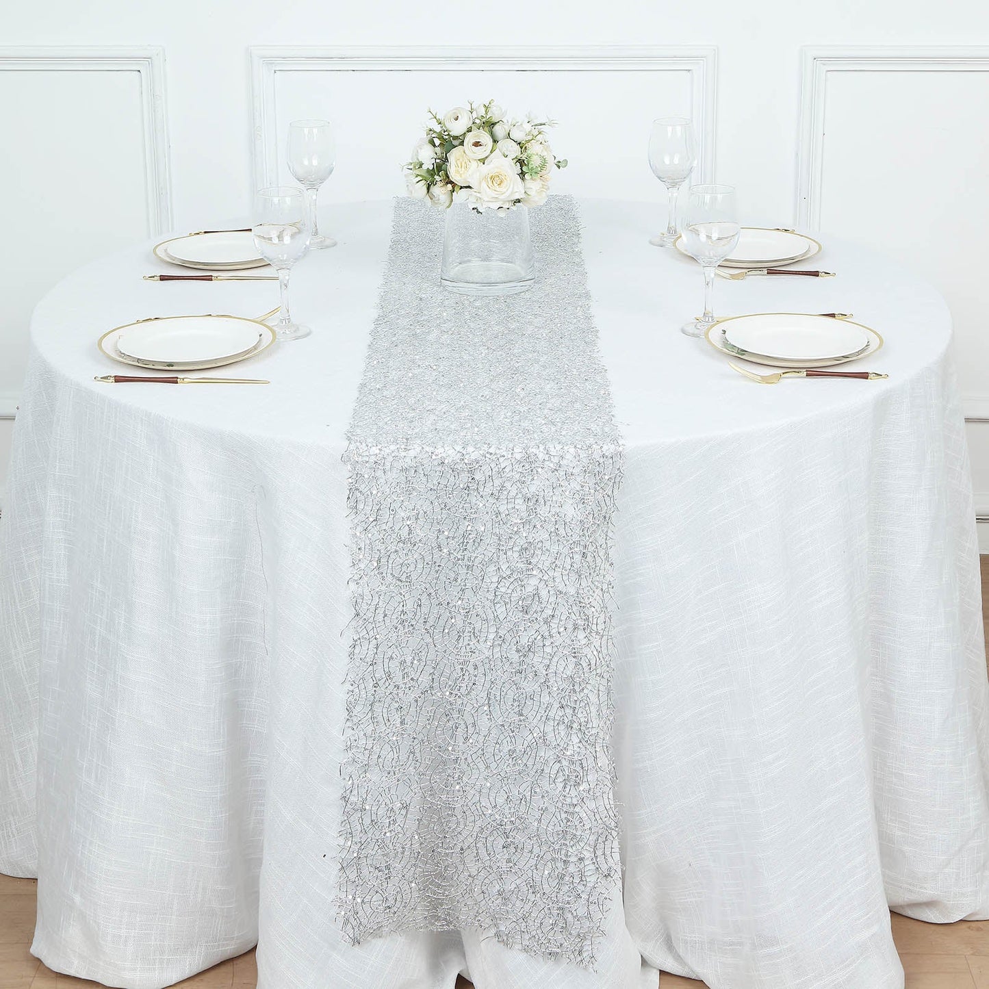 Silver sequin mesh lace table runner on a round table with floral centerpiece.