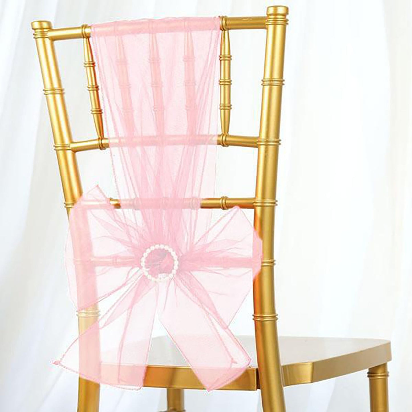 Blush sheer organza chair sash tied in a bow on a gold chair.