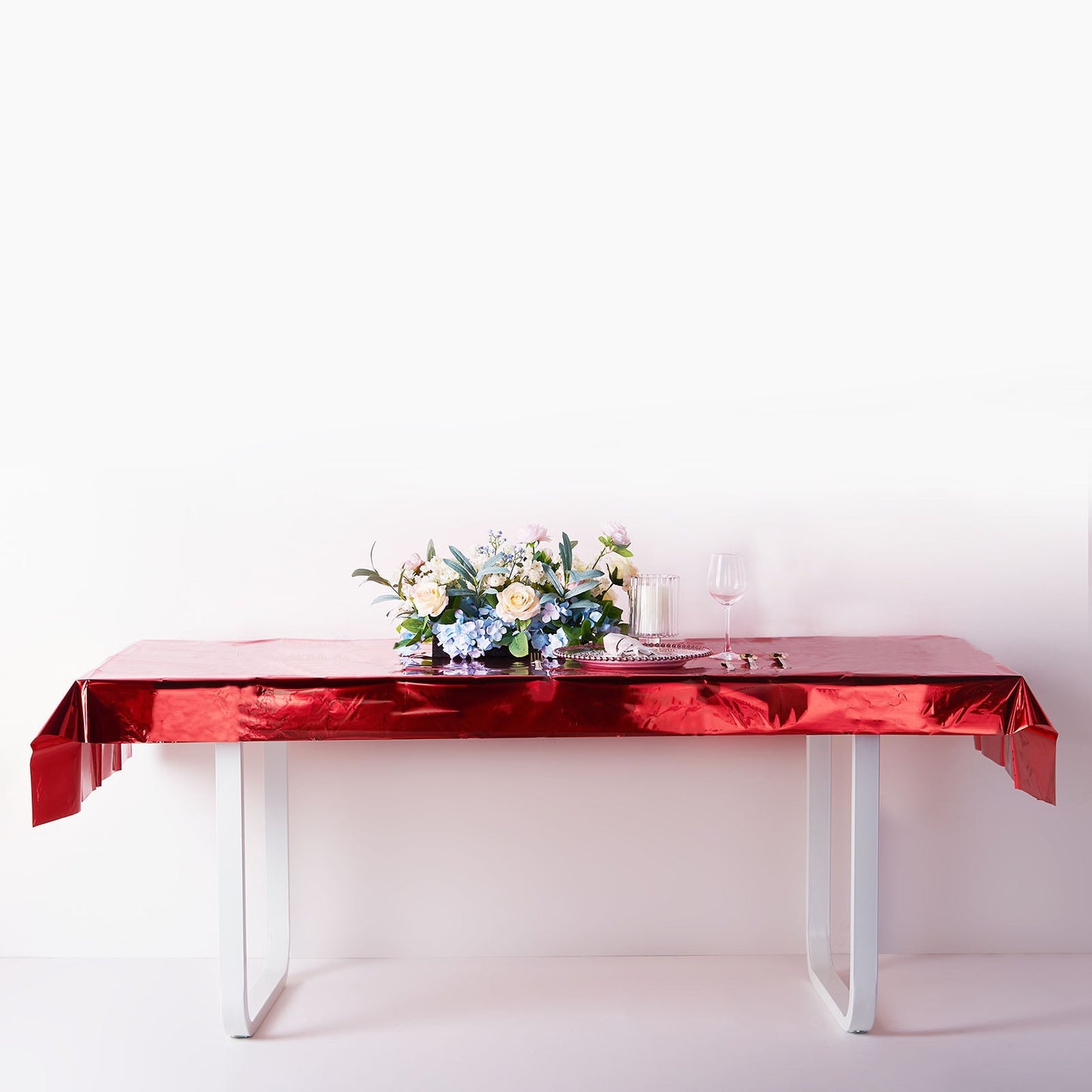 Red metallic foil rectangle tablecloth on a white table with floral centerpiece.