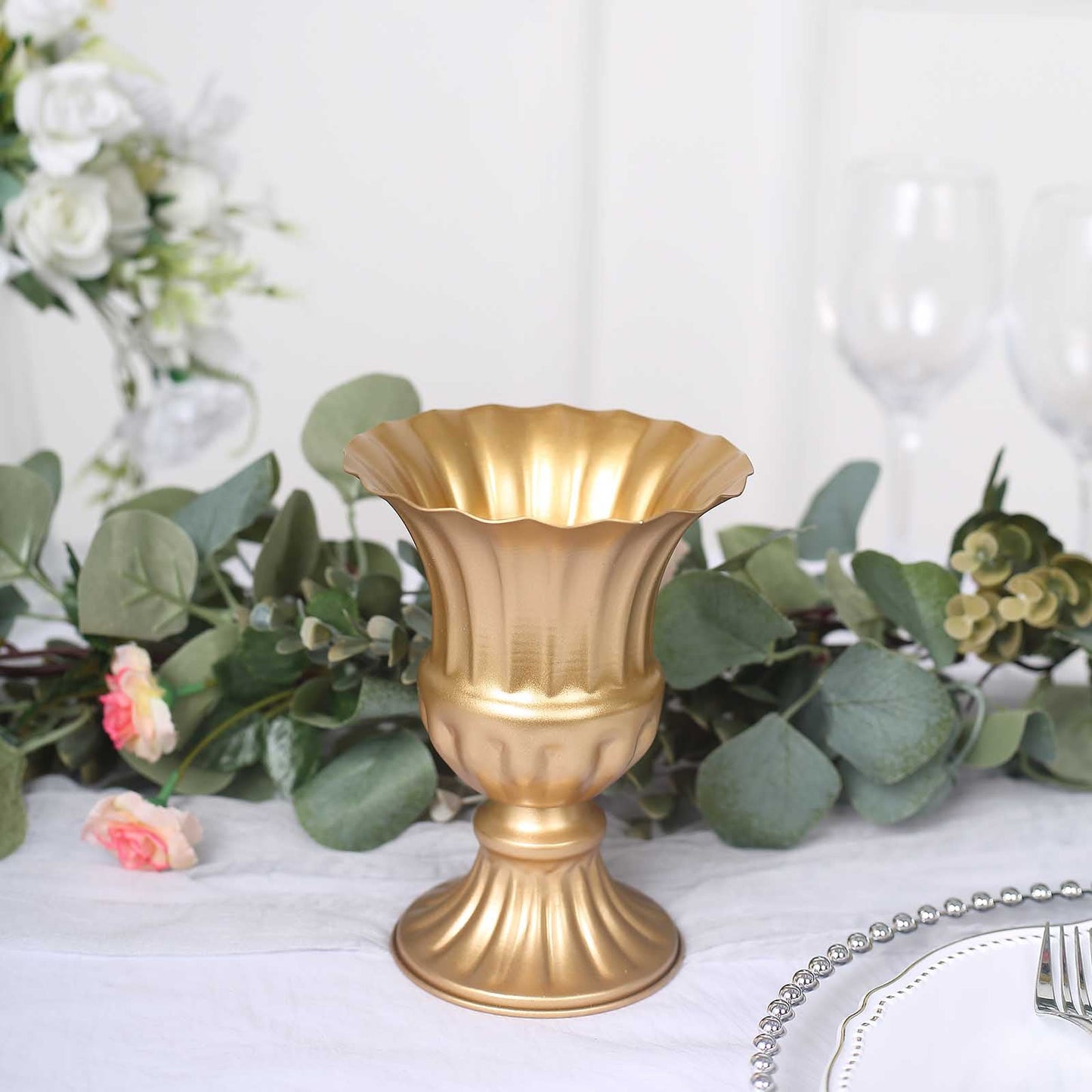 Gold metal trumpet style flower vase on a table with greenery and flowers.