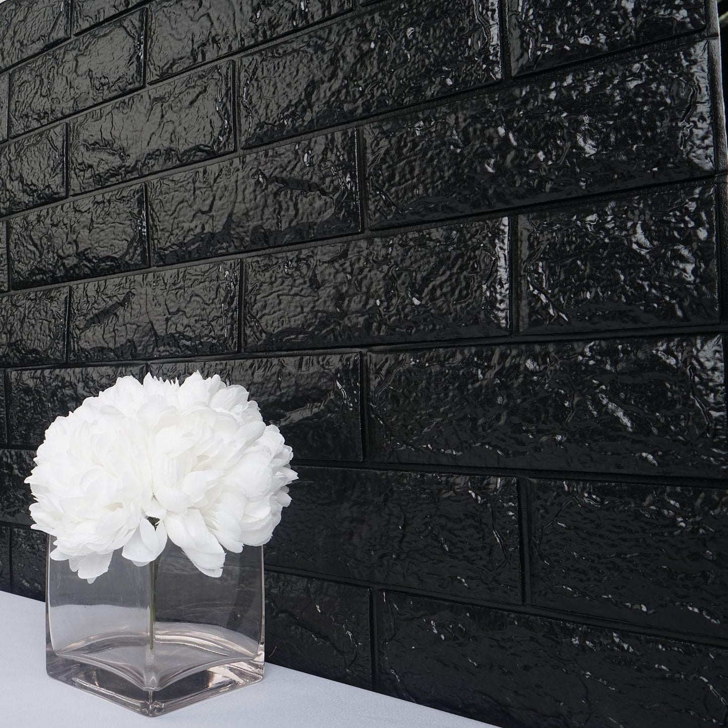 Black foam brick peel and stick 3D wall tile panels with white flowers in a vase.