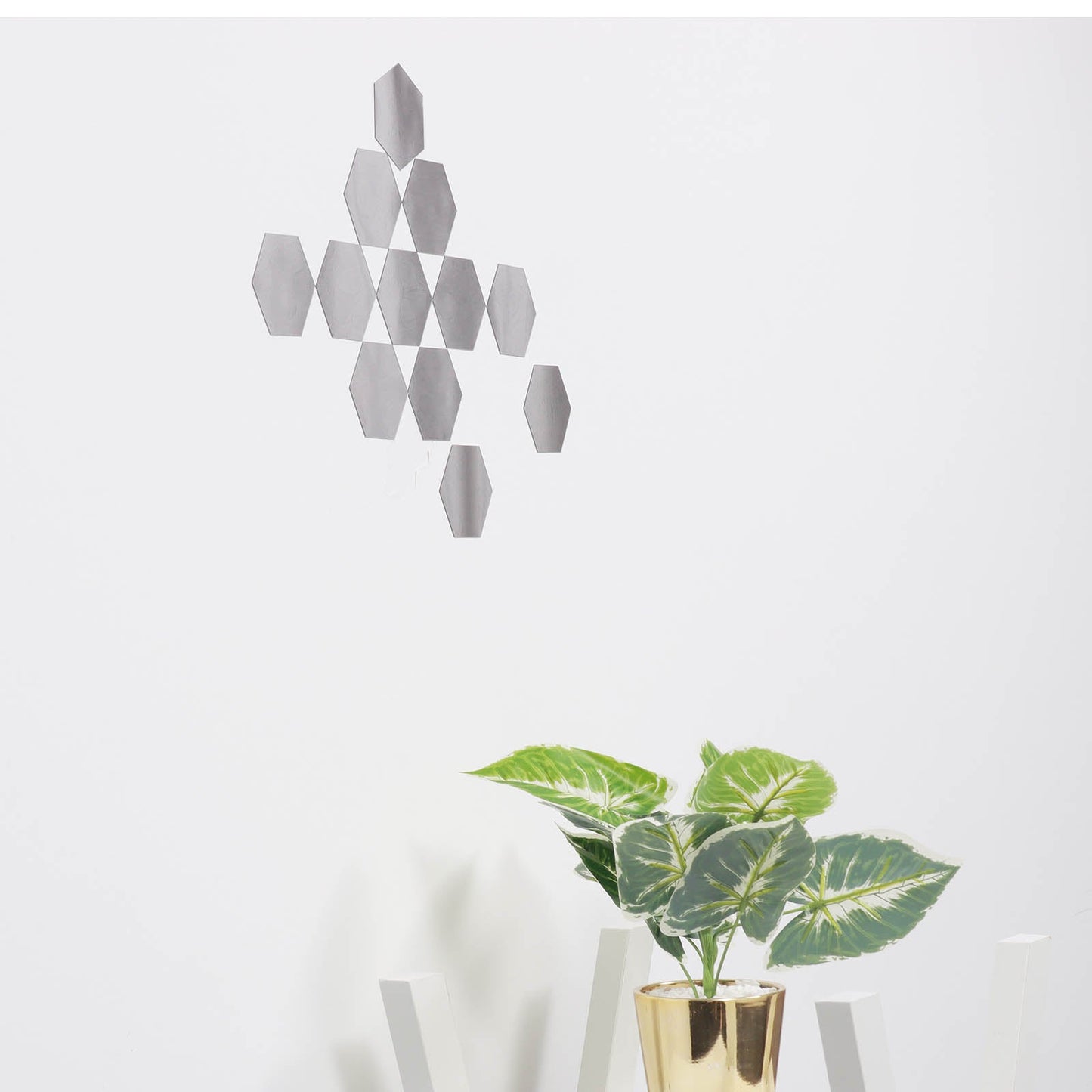 Silver hexagon mirror wall stickers on a white wall, with a plant below.