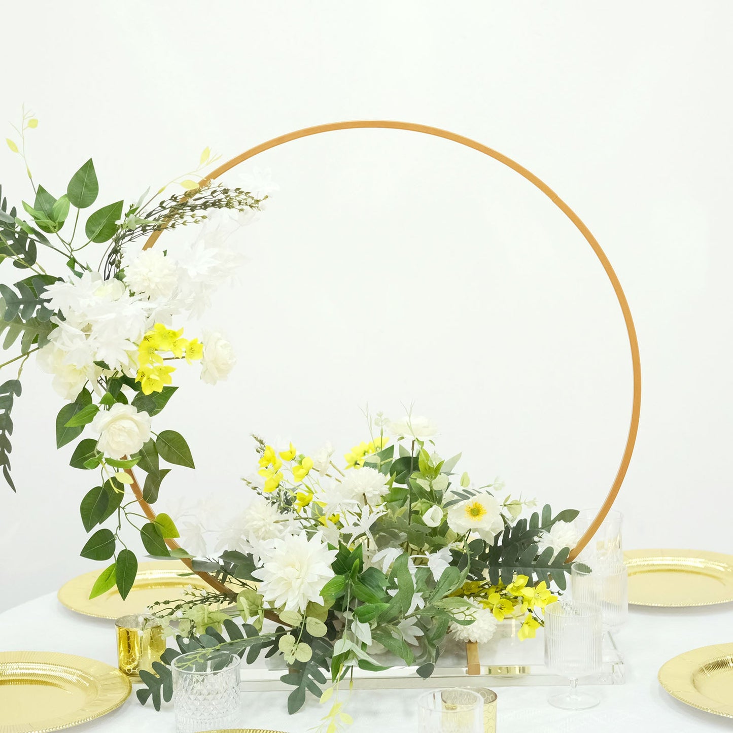 Gold metal round hoop floral centerpiece with white and yellow flowers.