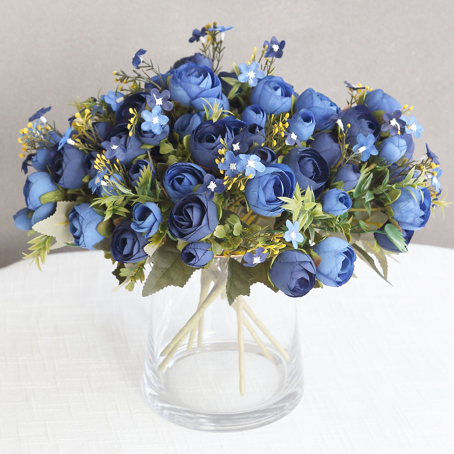 Navy blue artificial ranunculus flower bouquet in a glass vase.