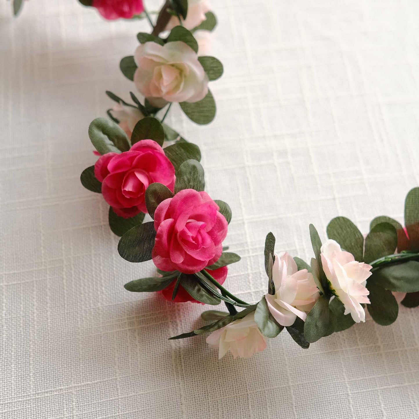 Blush fuchsia artificial silk flower garland with mini roses and green leaves.
