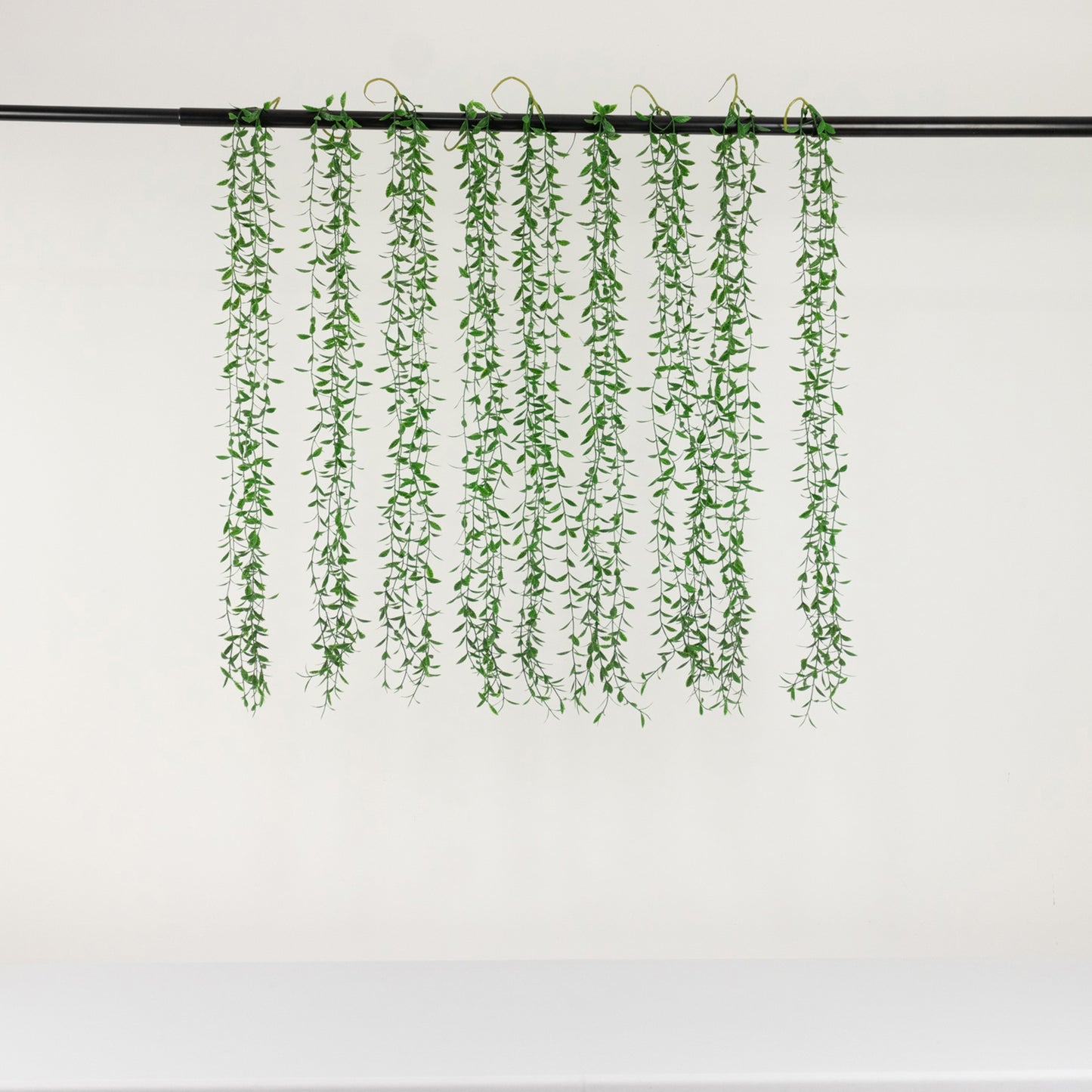 Green artificial hanging vines with weeping willow leaves for decor.