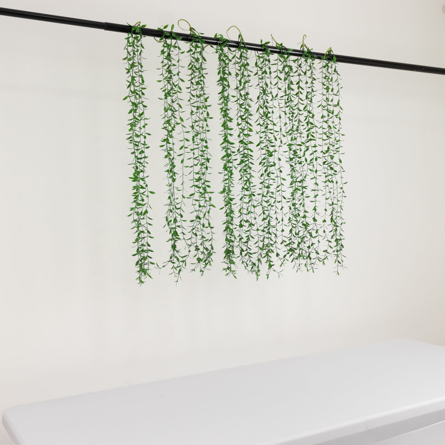 Green artificial hanging vines with weeping willow leaves for wall decor.