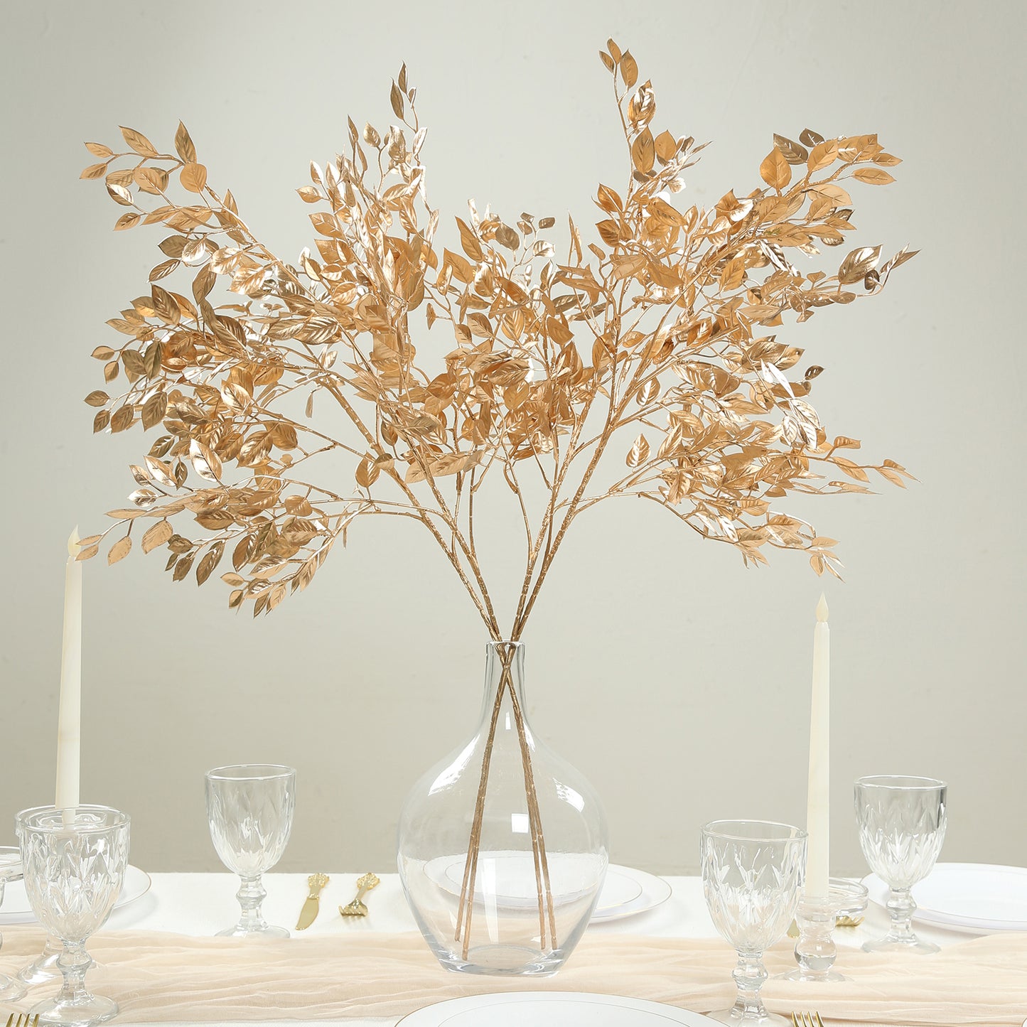 Gold metallic artificial leaf spray arrangement in a clear vase.
