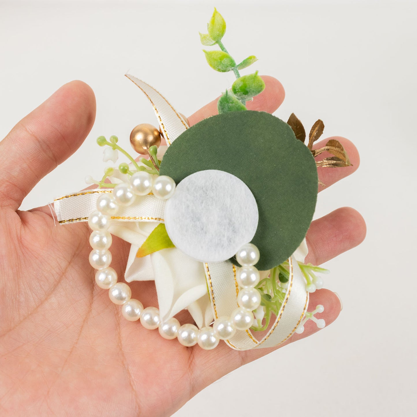White artificial rose wrist corsage with pearls and greenery. Wedding accessory.