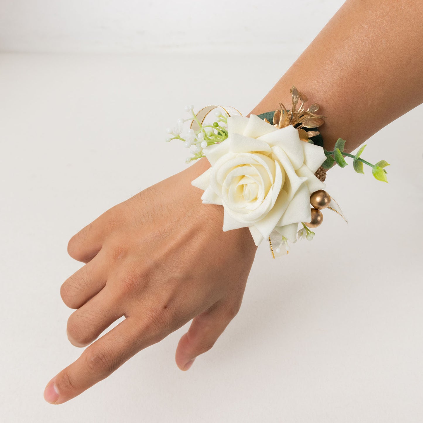 White artificial rose wrist corsage with pearls and greenery for weddings.