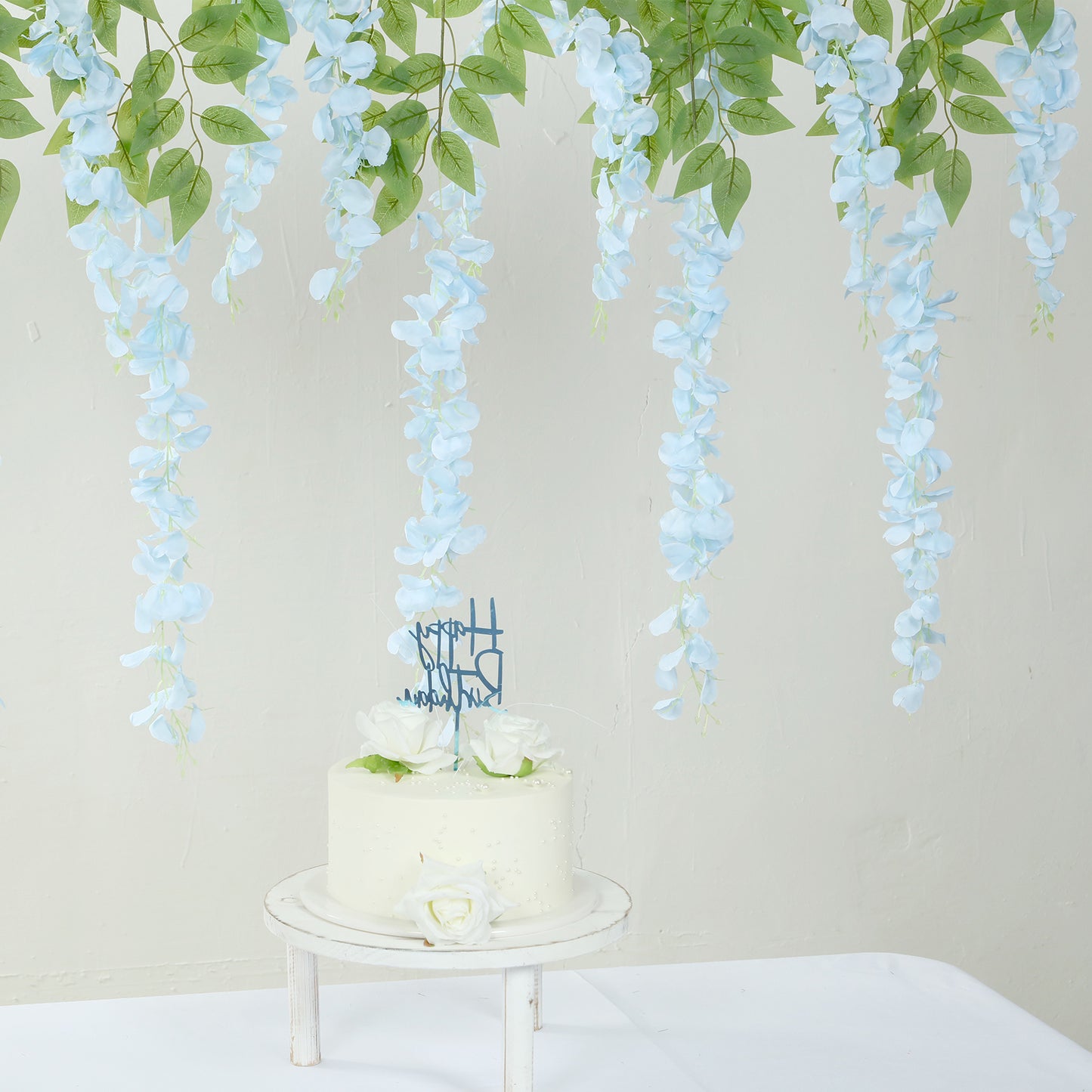 Light blue silk hanging wisteria flower garland above a white cake.