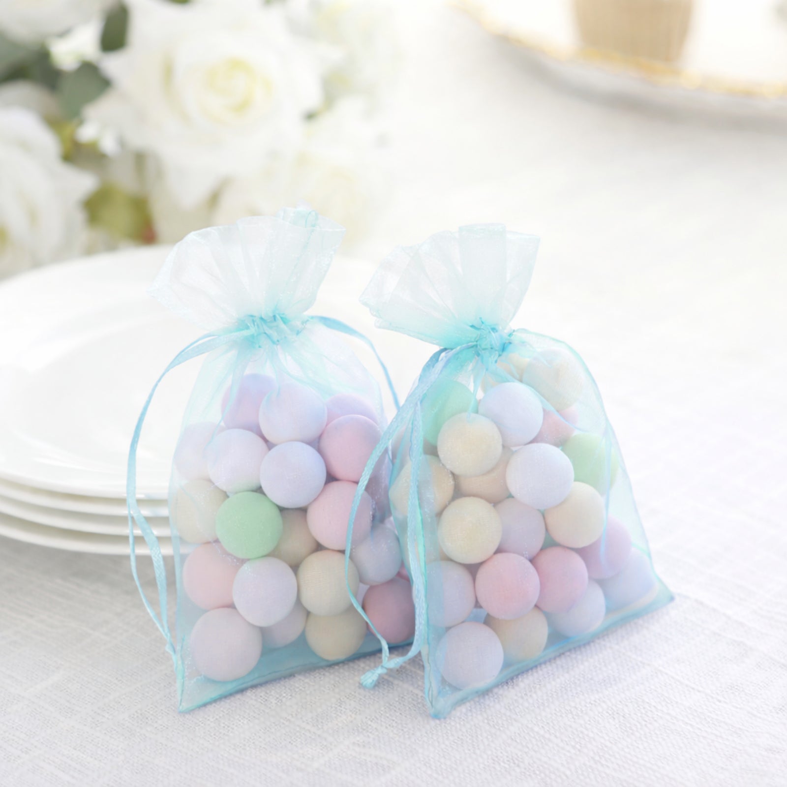 Light blue organza gift bags with drawstring, filled with pastel candies.