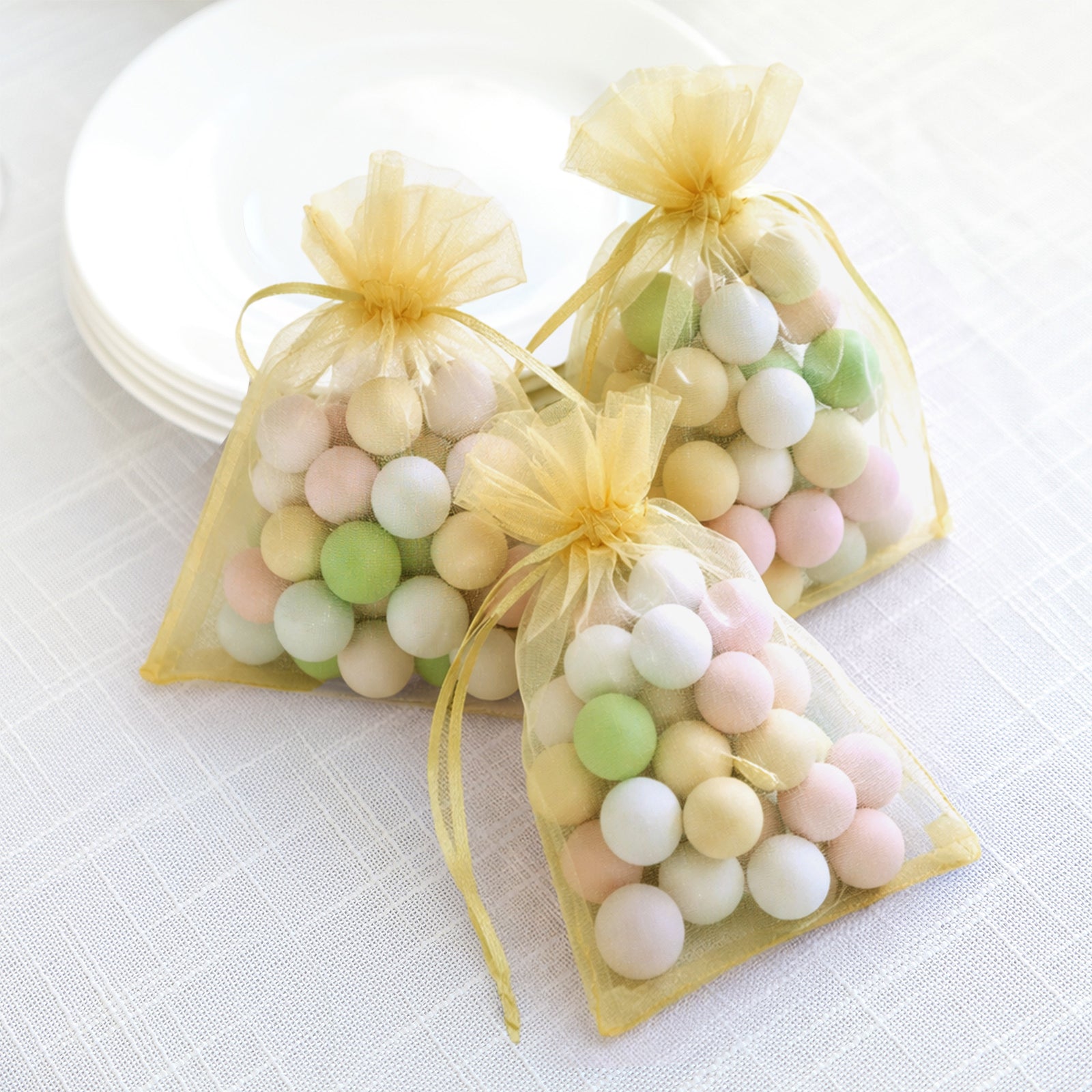 Gold organza gift bags with drawstring containing pastel candies.