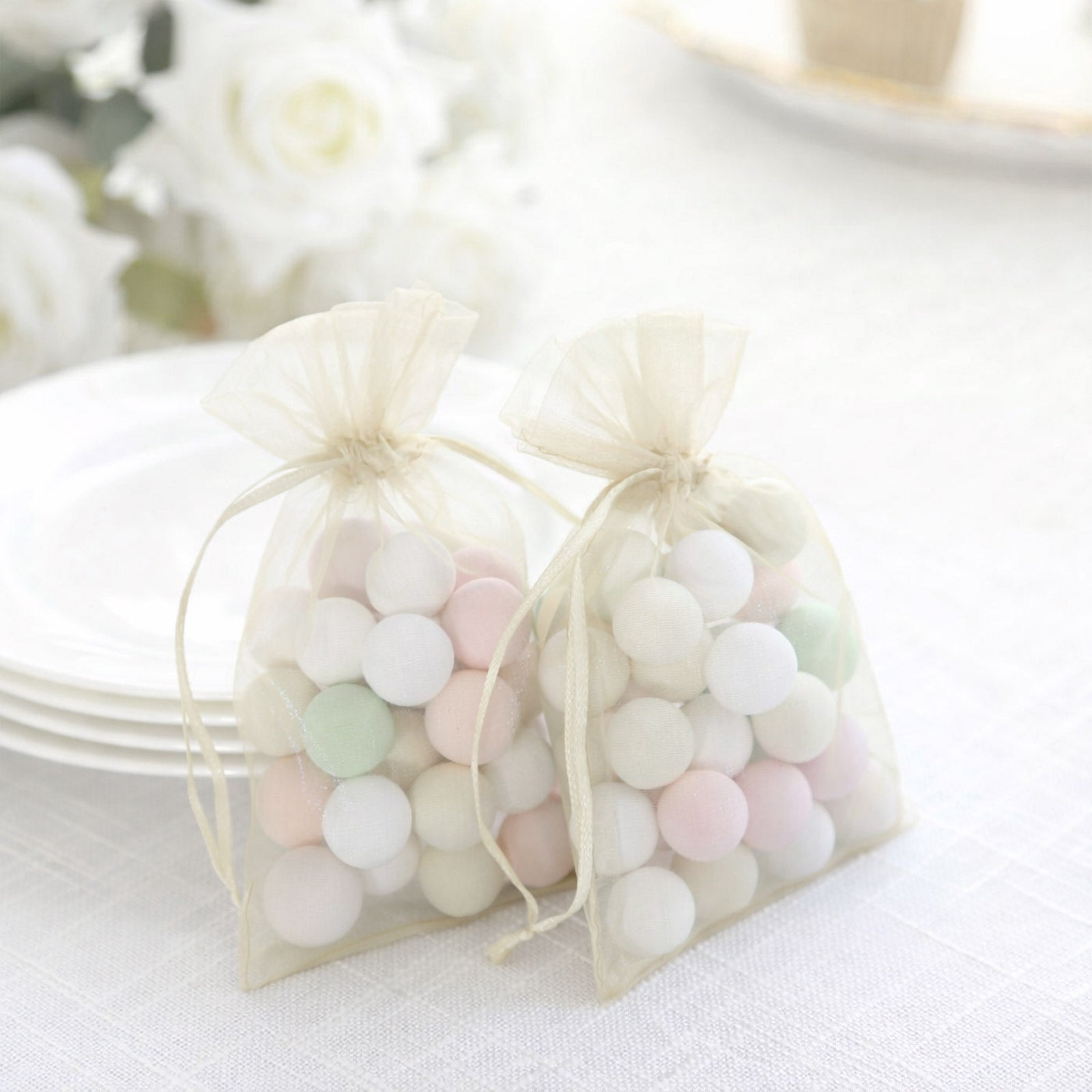 Ivory organza gift bags with drawstring, filled with pastel candies.
