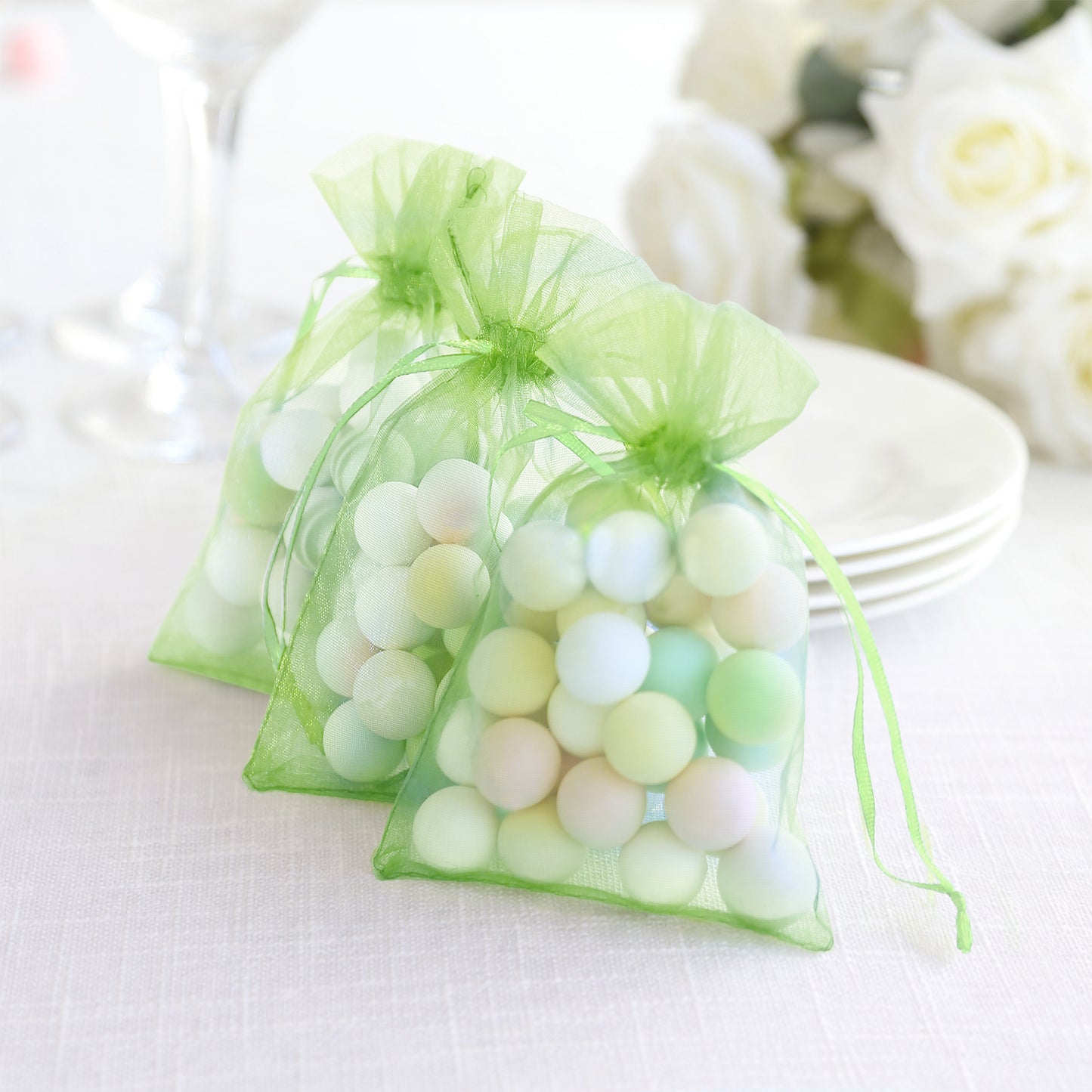 Mint organza gift bags with drawstring, filled with colorful round favors.