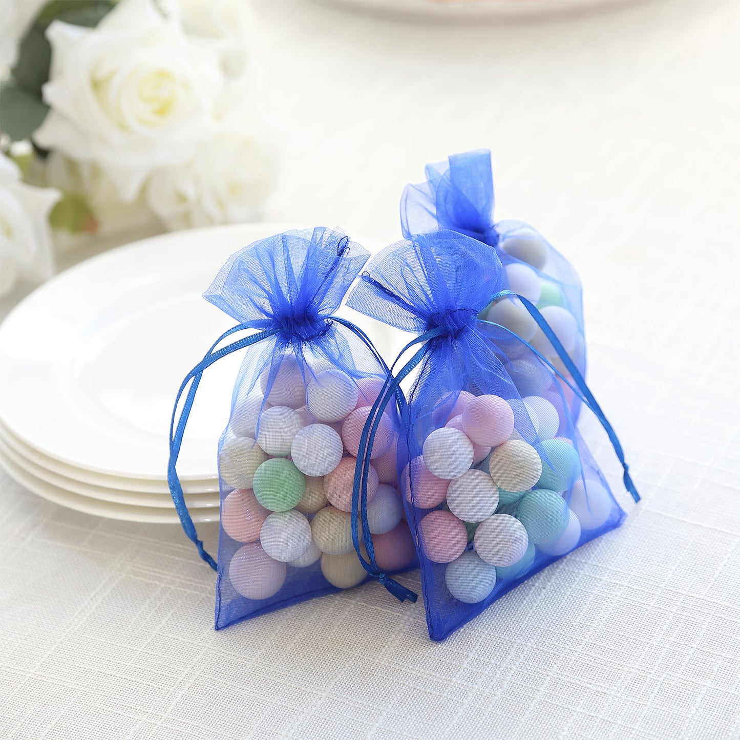 Royal blue organza gift bags with drawstring, filled with colorful round candies.