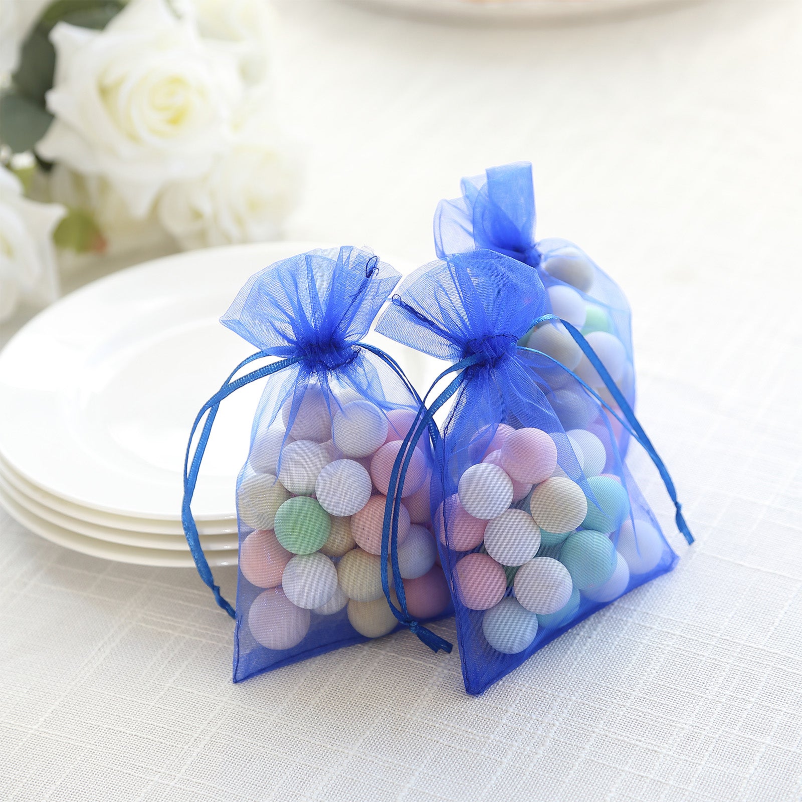 Royal blue organza gift bags with drawstring, filled with colorful round candies.
