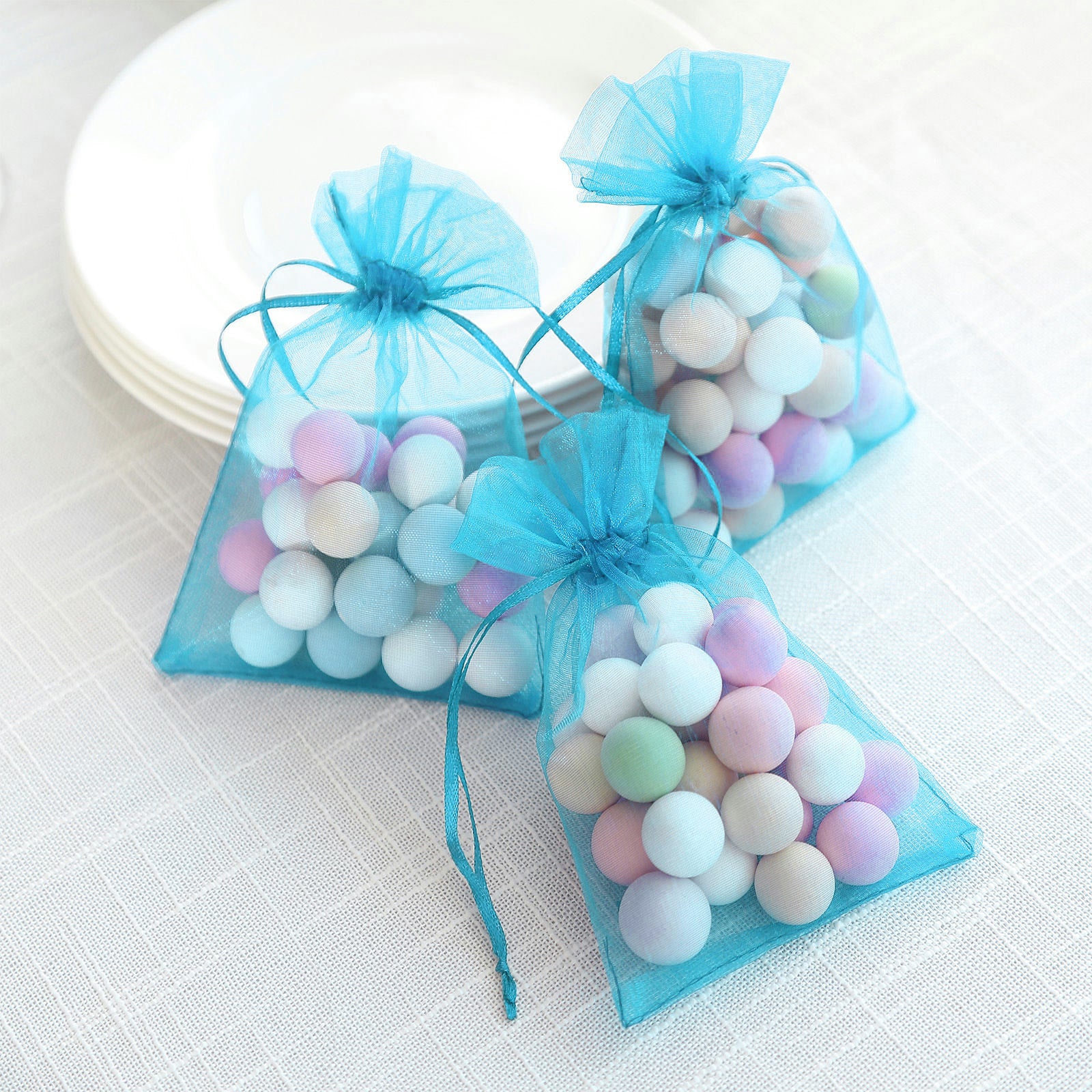 Turquoise organza gift bags with drawstring, filled with colorful candies.