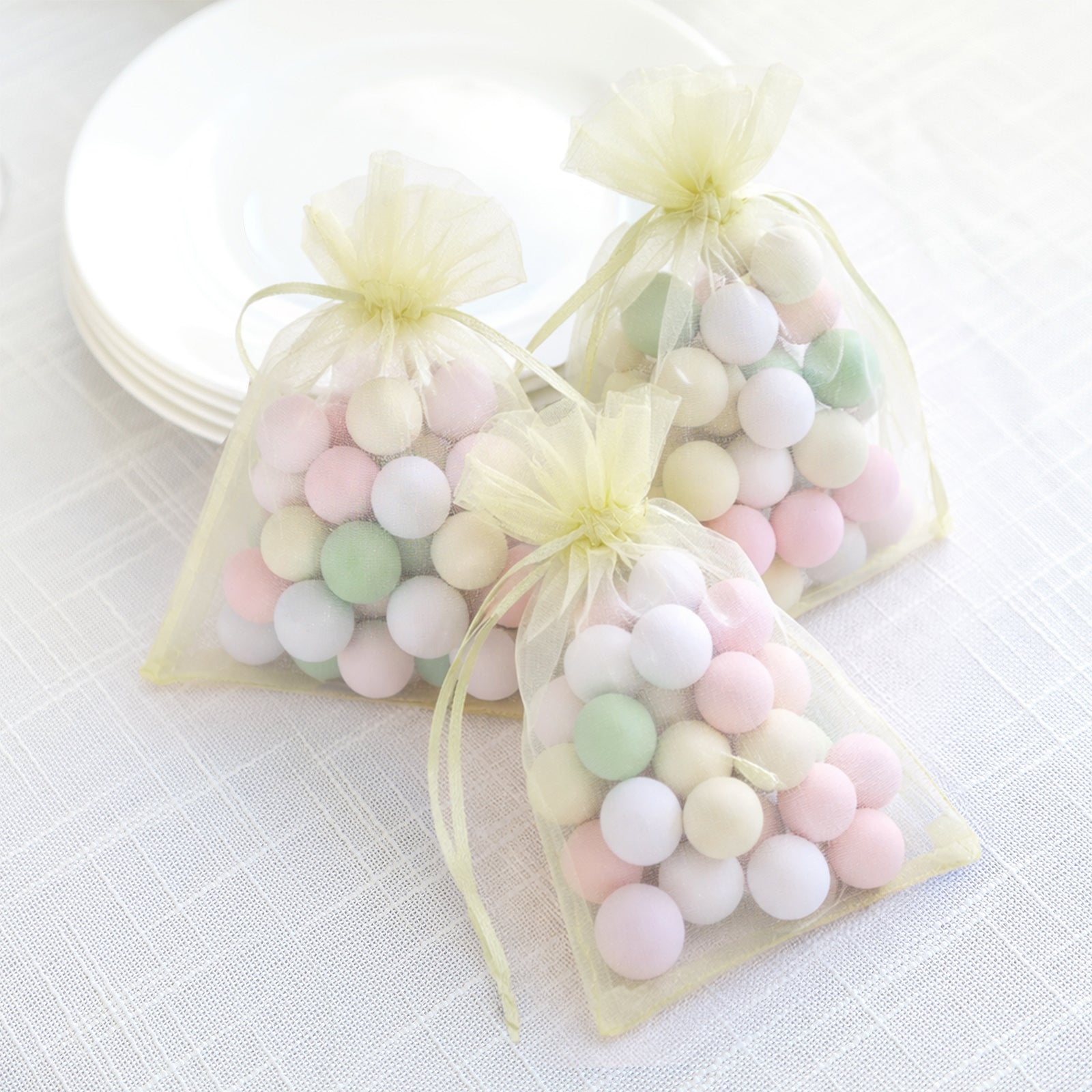 Yellow organza gift bags with drawstring filled with pastel balls.