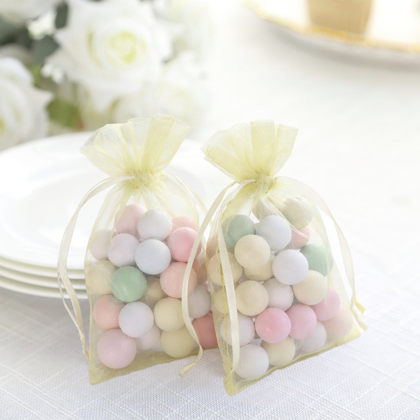 Yellow organza gift bags with pastel candies inside, perfect for party favors.