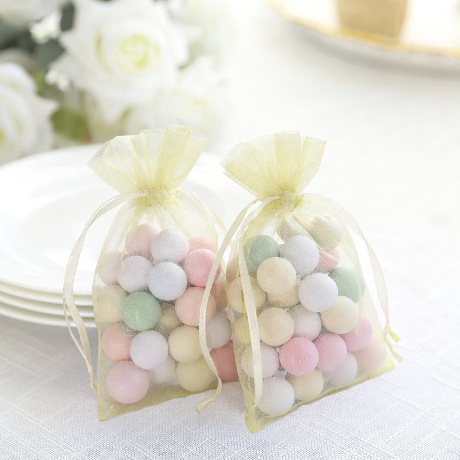 Yellow organza gift bags with pastel candies inside, perfect for party favors.