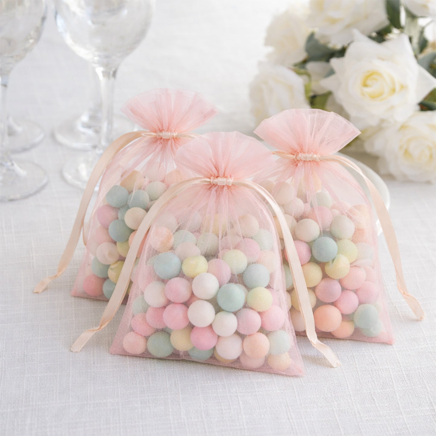 Blush organza gift bags filled with pastel candies for wedding favors.