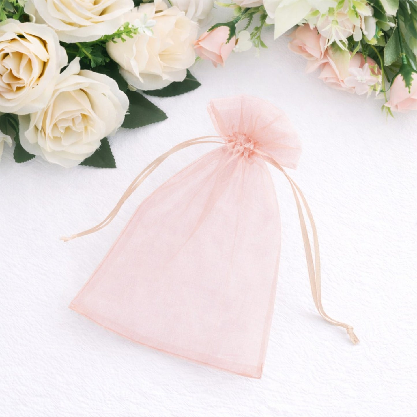 Blush organza gift bag with drawstring among flowers.