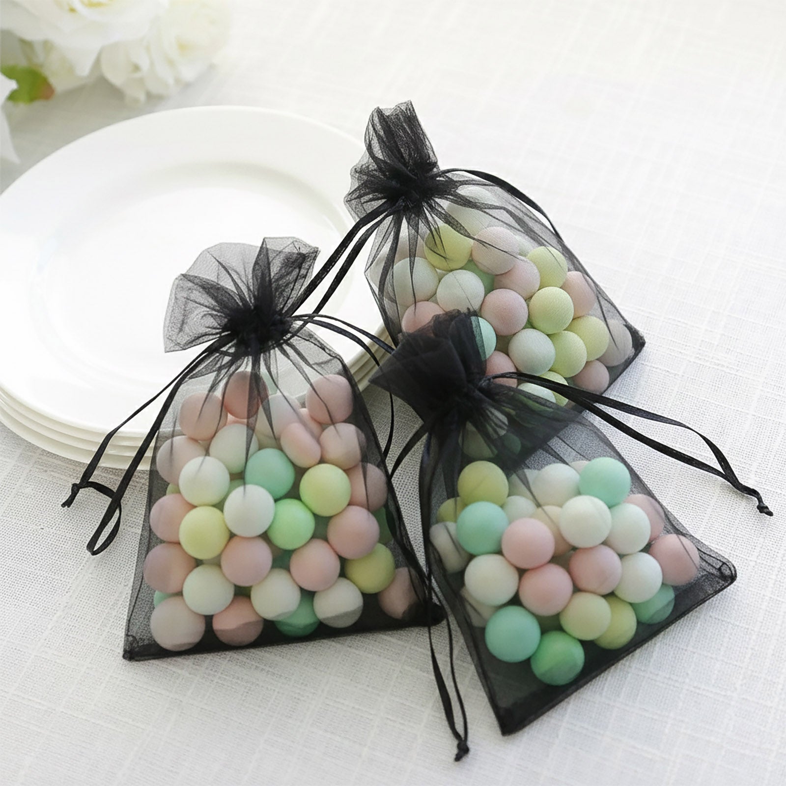 Black organza gift bags with drawstring filled with colorful candies.