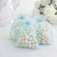 Light blue organza gift bags with drawstring filled with pastel candies.