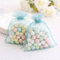 Light blue organza gift bags with drawstring, filled with pastel candies.
