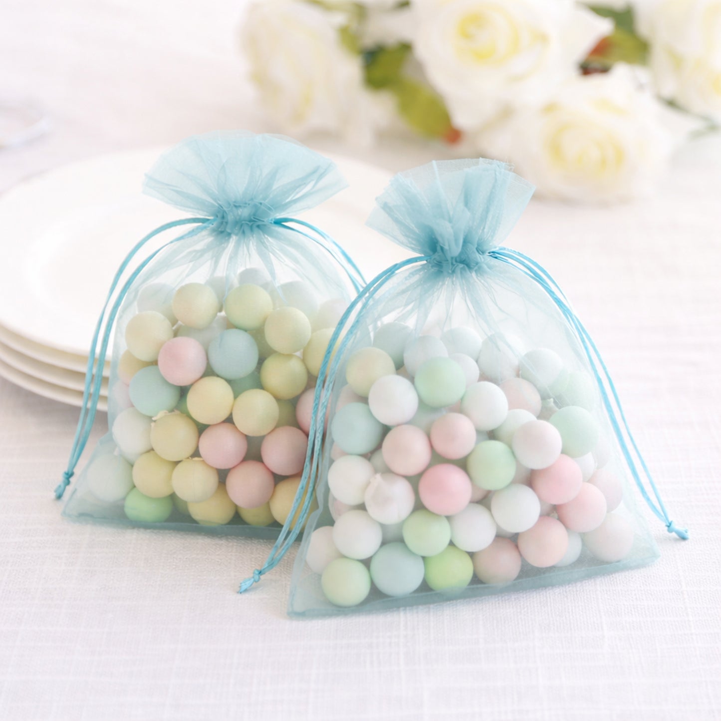 Light blue organza gift bags with drawstring, filled with pastel candies.