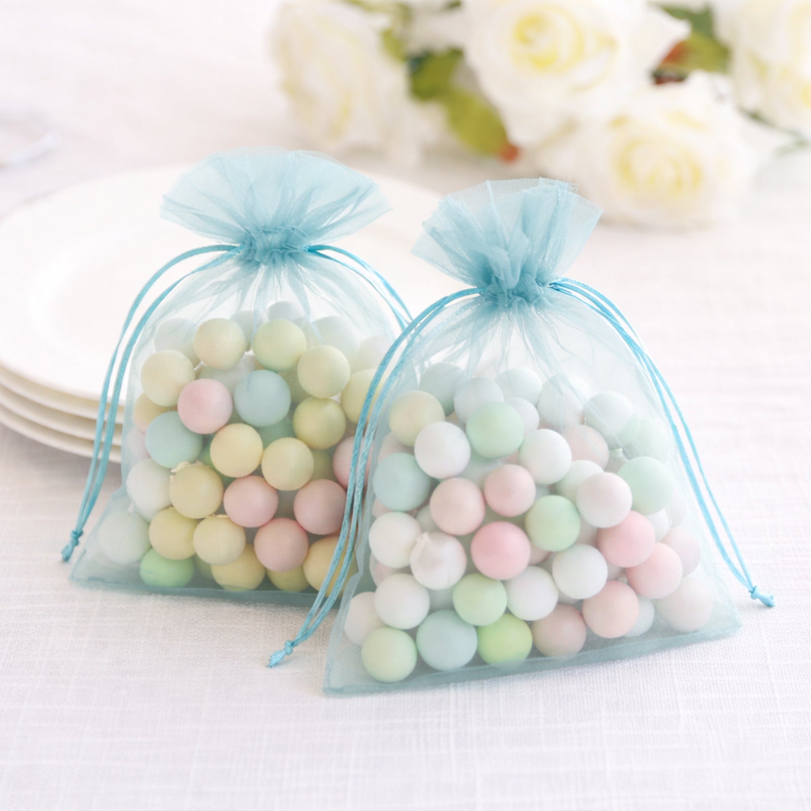 Light blue organza gift bags with drawstring, filled with pastel candies.
