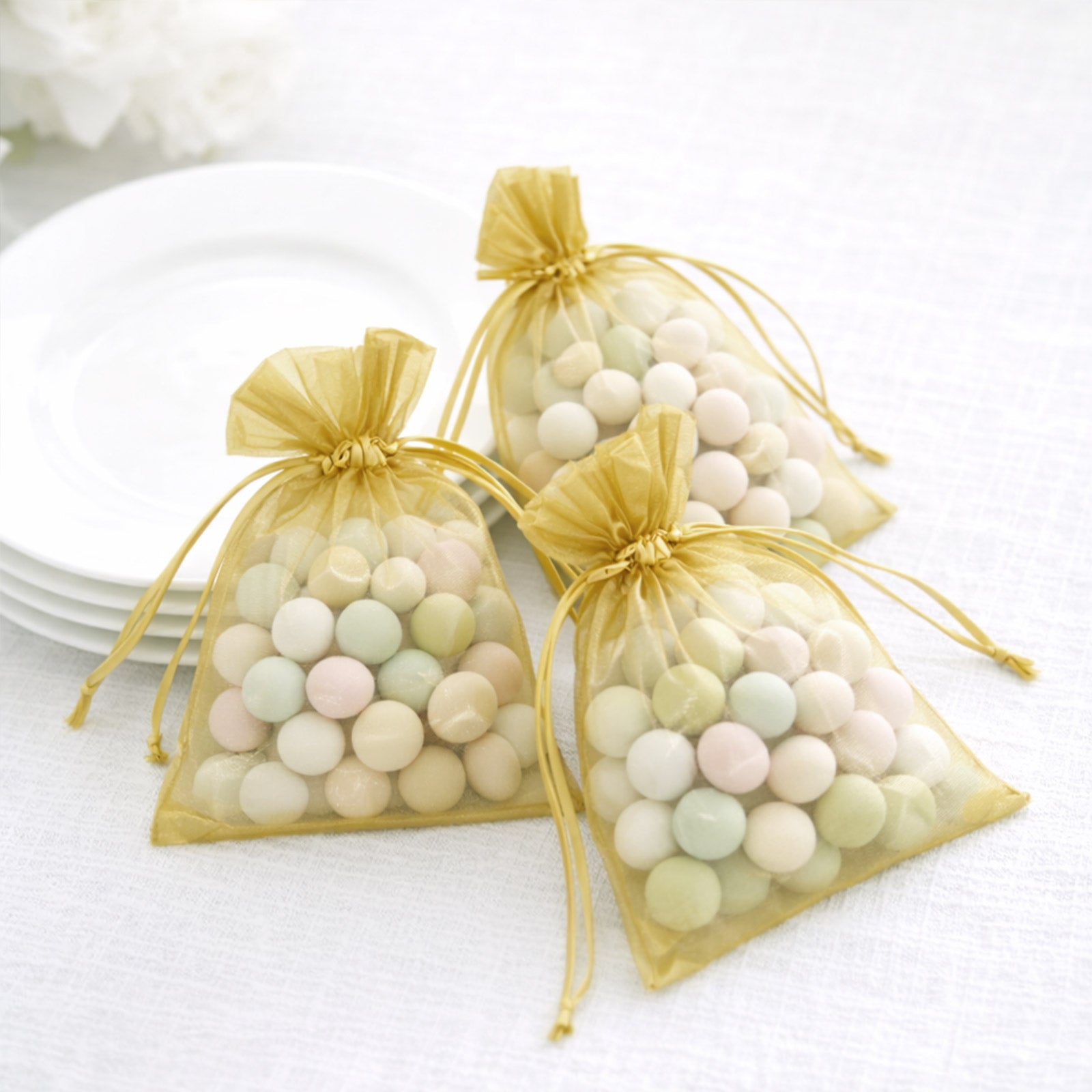 Gold organza gift bags with drawstring filled with colorful candies.