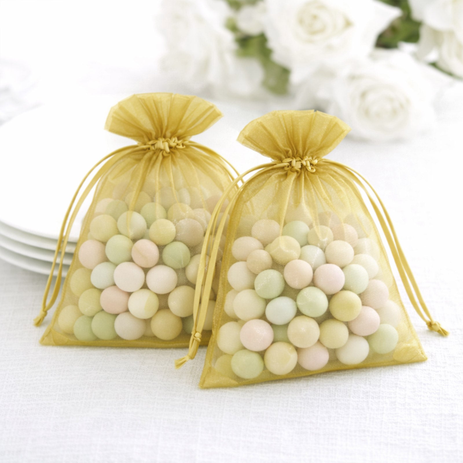 Gold organza gift bags filled with pastel candies, perfect for wedding favors.