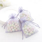 Lavender organza gift bags with drawstring, filled with pastel candies.