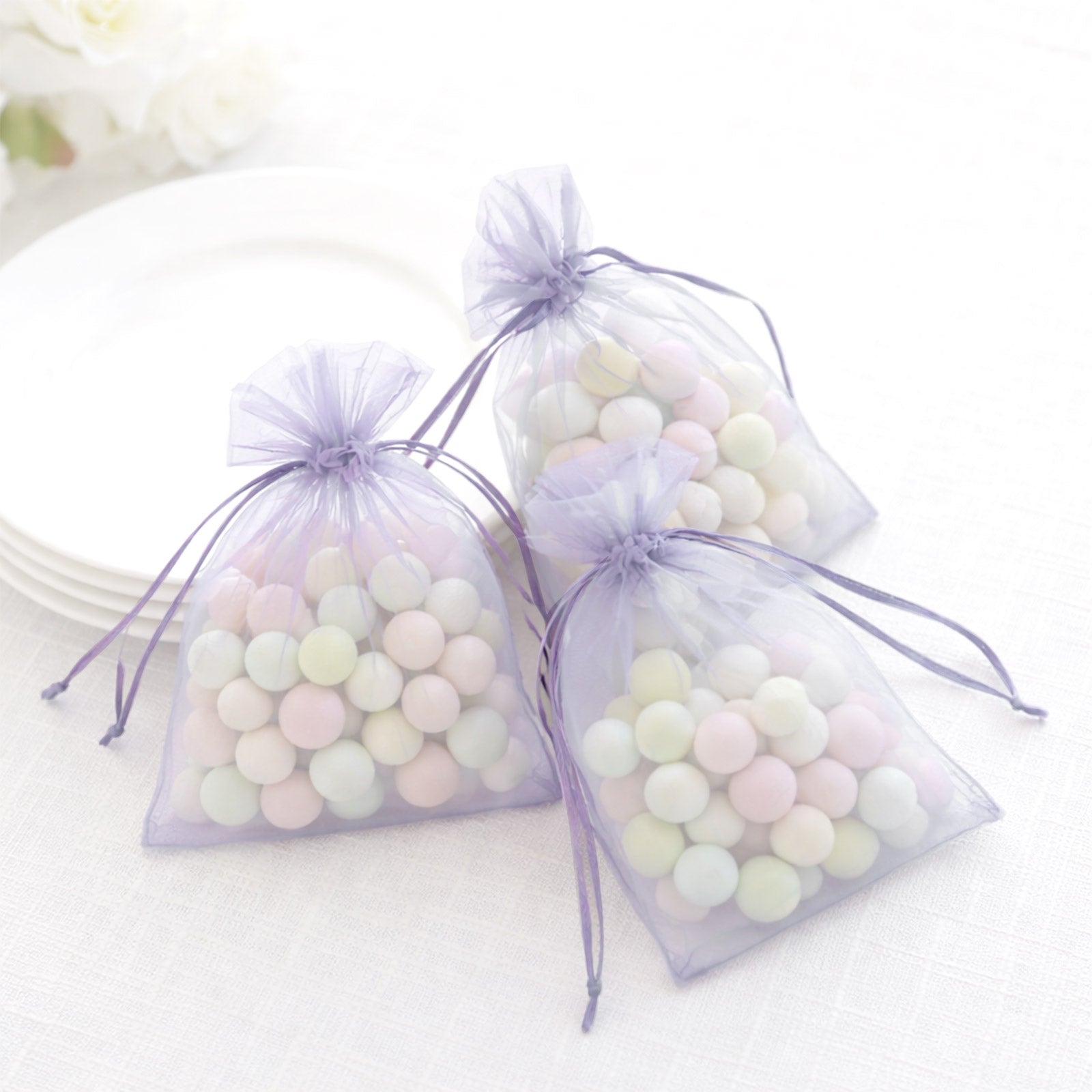 Lavender organza gift bags with drawstring, filled with pastel candies.