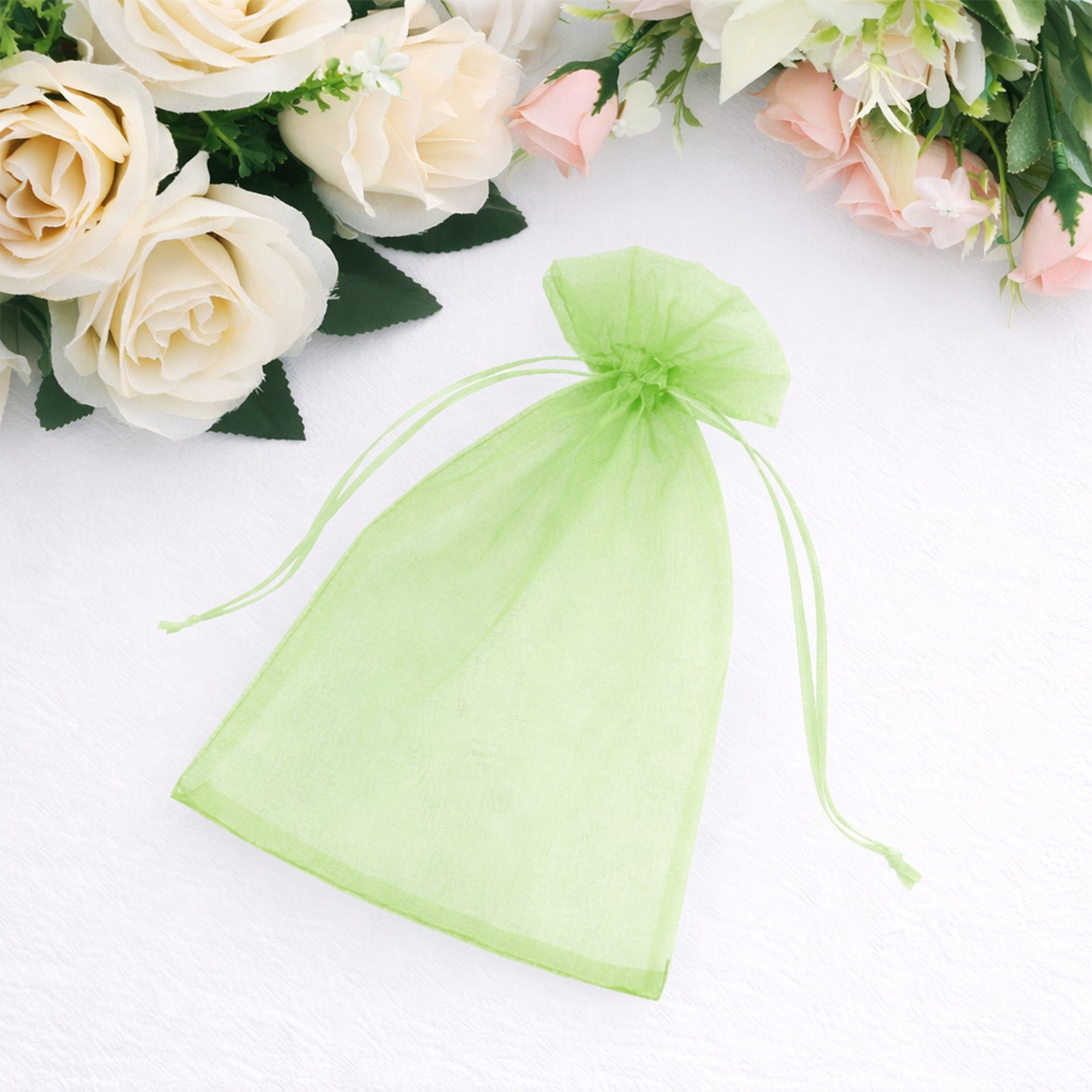 Mint organza gift bag with drawstring among floral decorations.