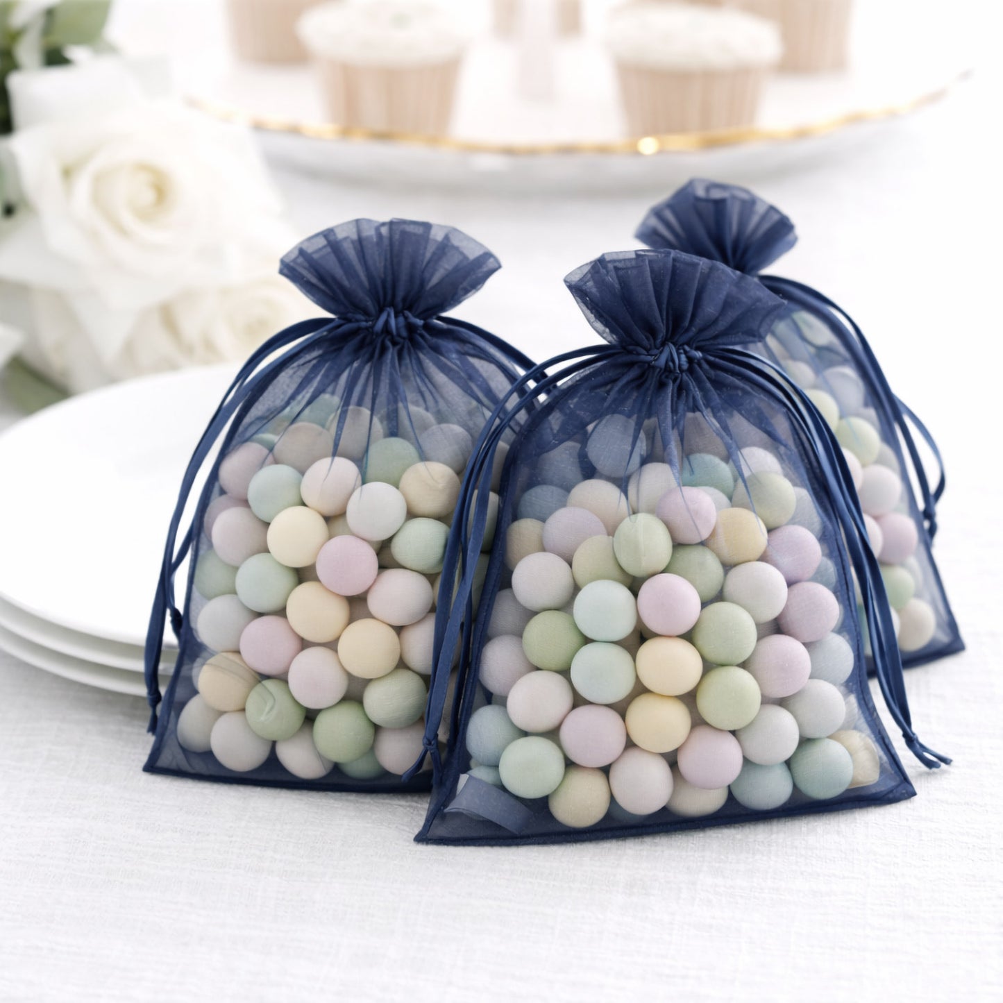 Navy blue organza gift bags filled with pastel candies on a table setting.