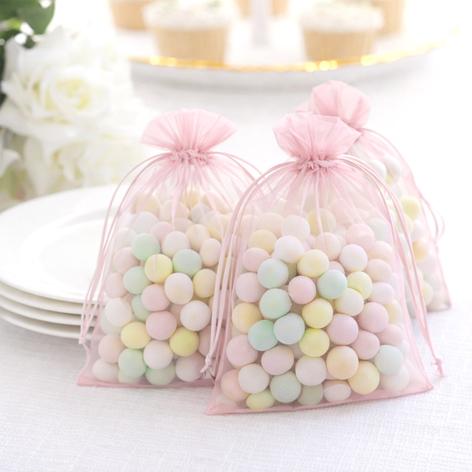 Pink organza gift bags with drawstring, filled with pastel candies.