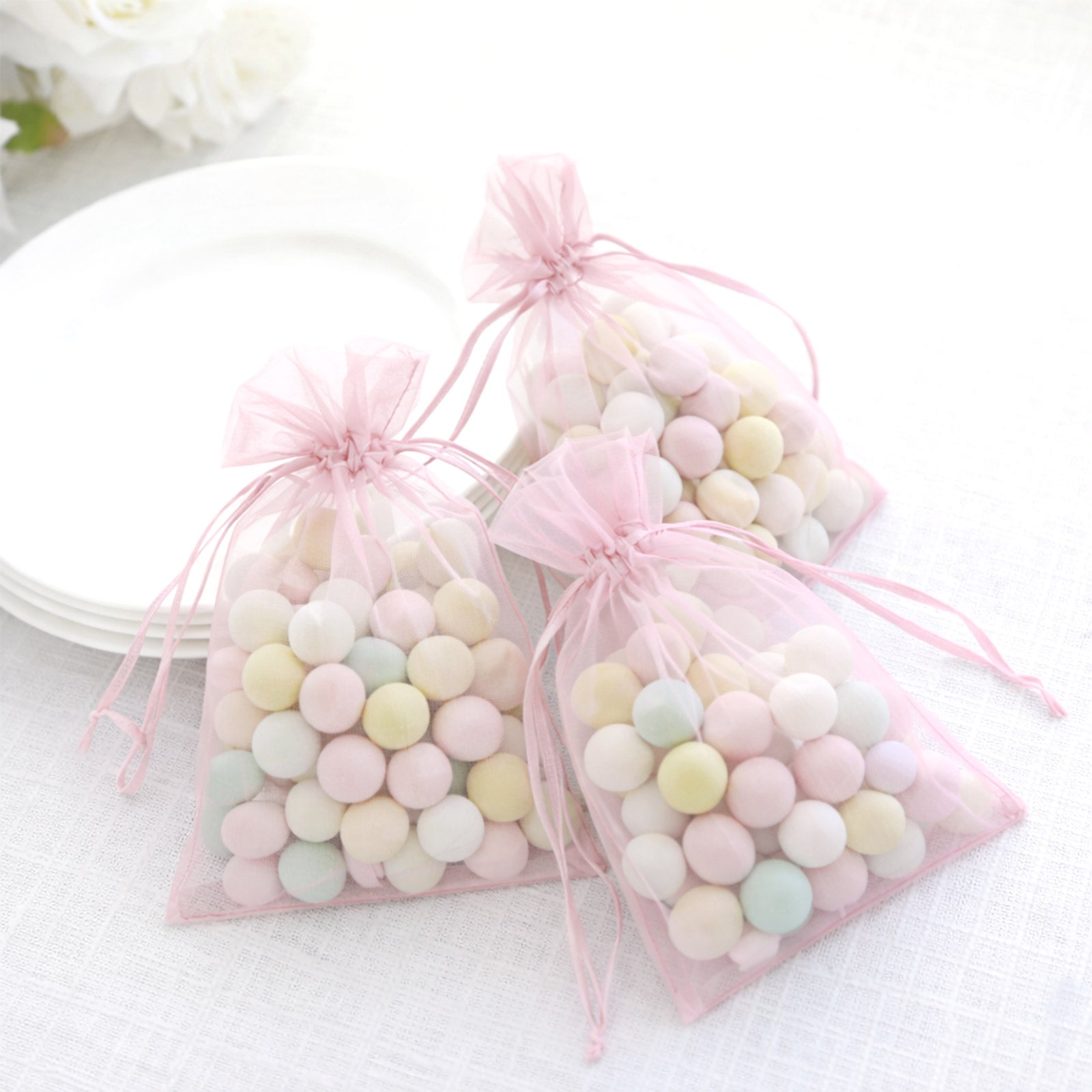 Pink organza gift bags with drawstring filled with pastel candies.