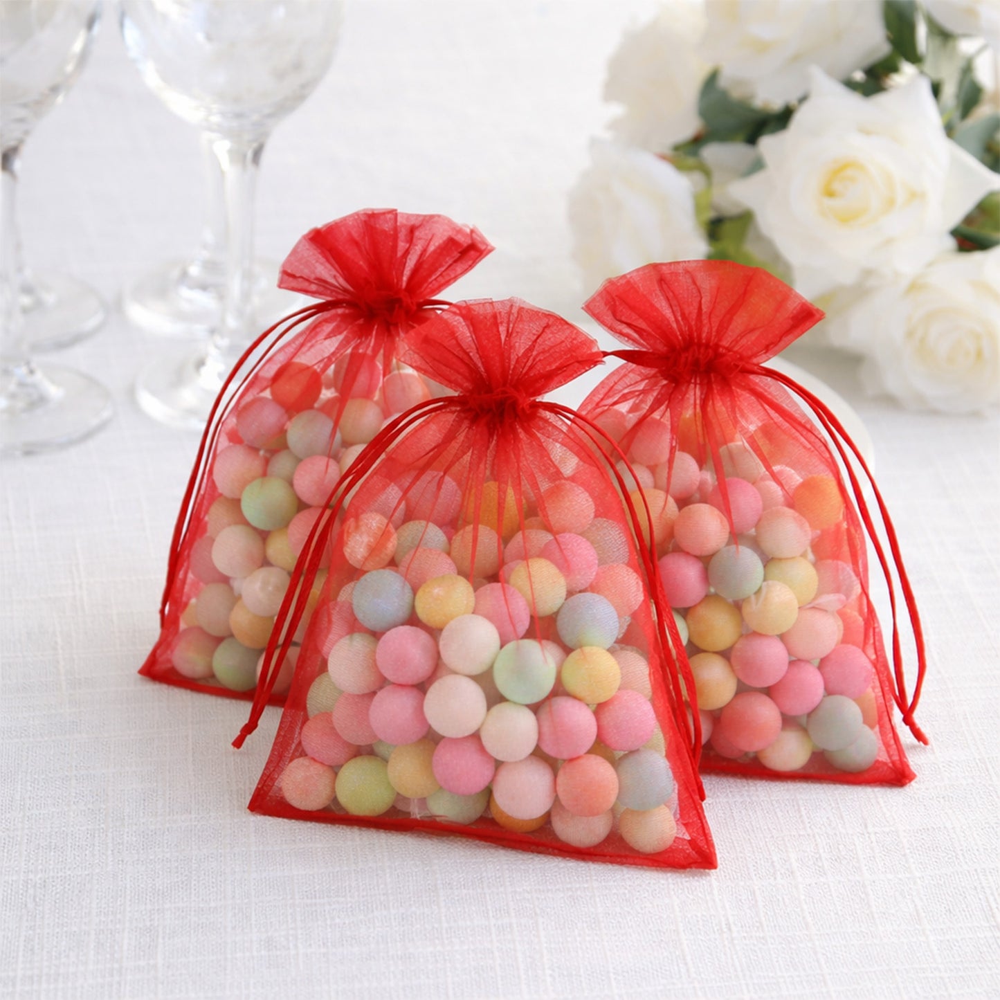 Red organza gift bags filled with colorful candies, perfect for weddings and parties.