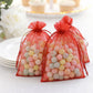 Red organza gift bags filled with colorful candies, perfect for party favors.