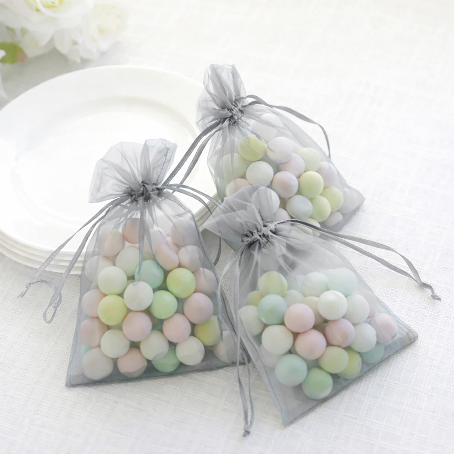 Silver organza gift bags with drawstring filled with pastel candies.