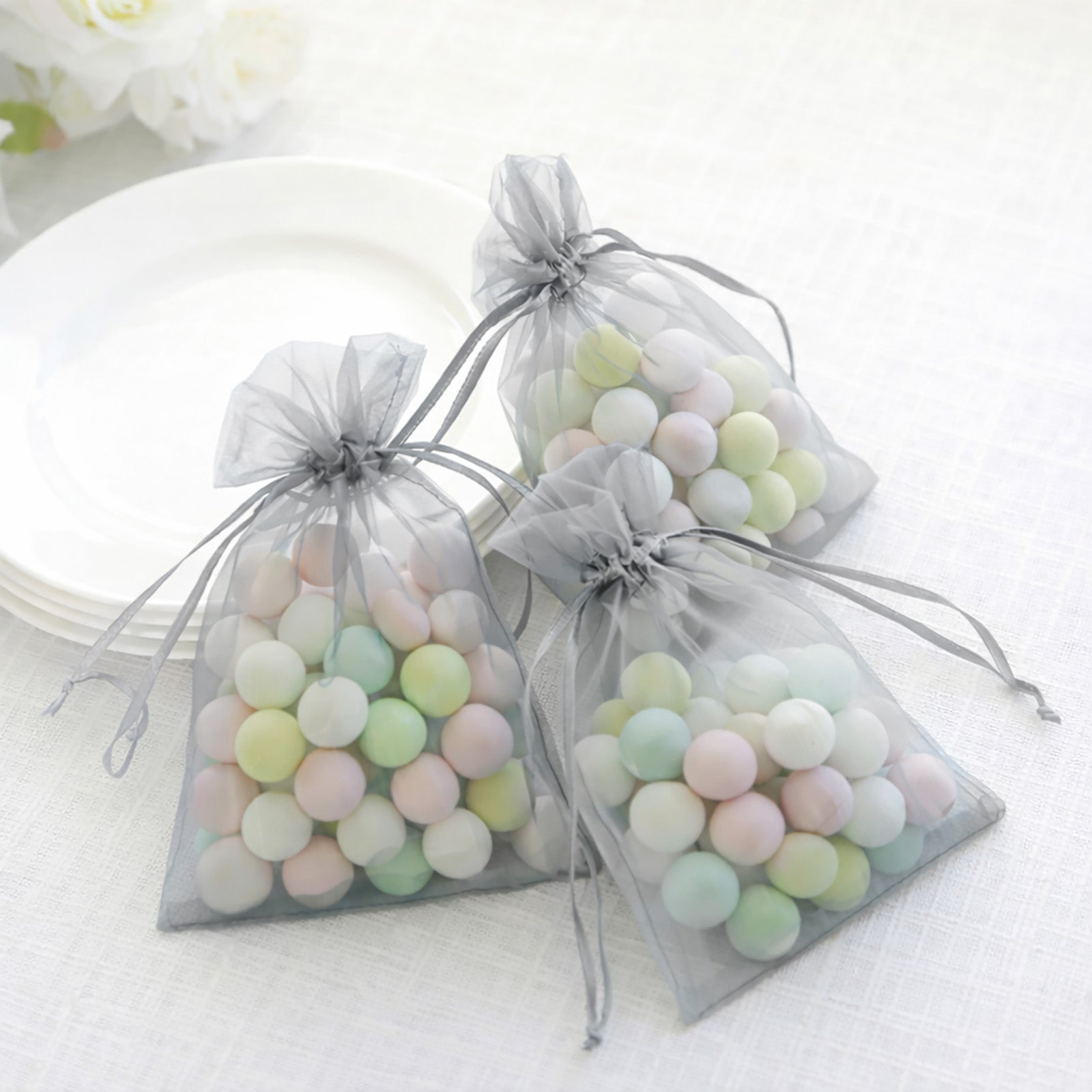 Silver organza gift bags with drawstring filled with pastel candies.