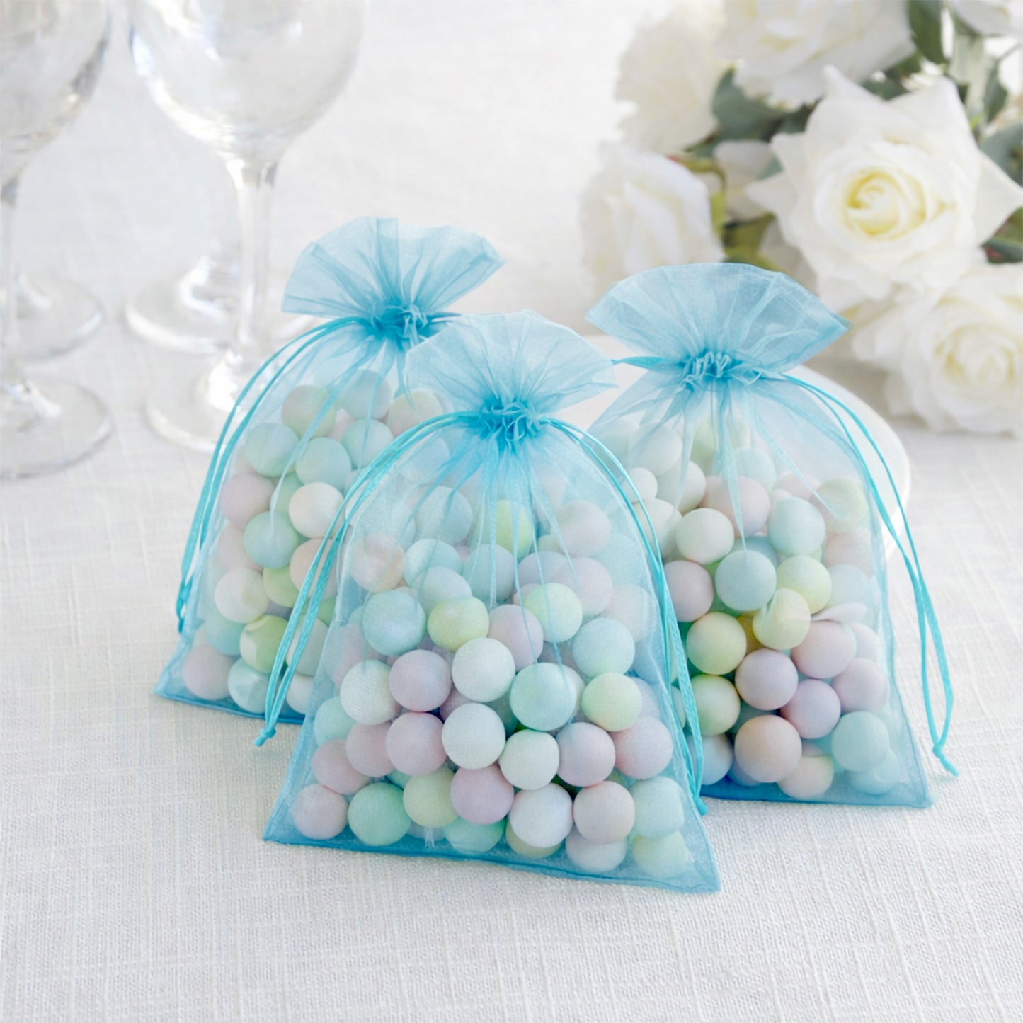 Turquoise organza gift bags filled with pastel candies, perfect for weddings.