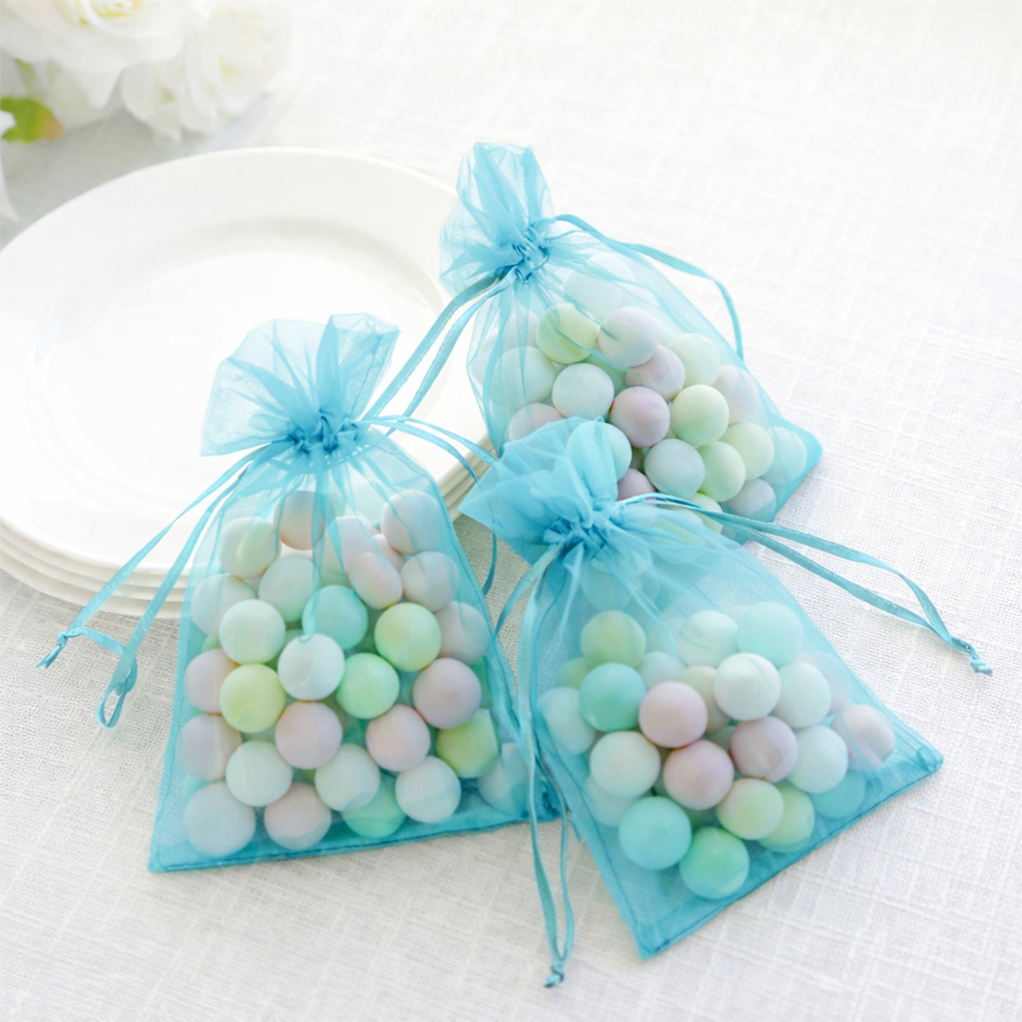Turquoise organza gift bags with drawstring, filled with colorful candies.