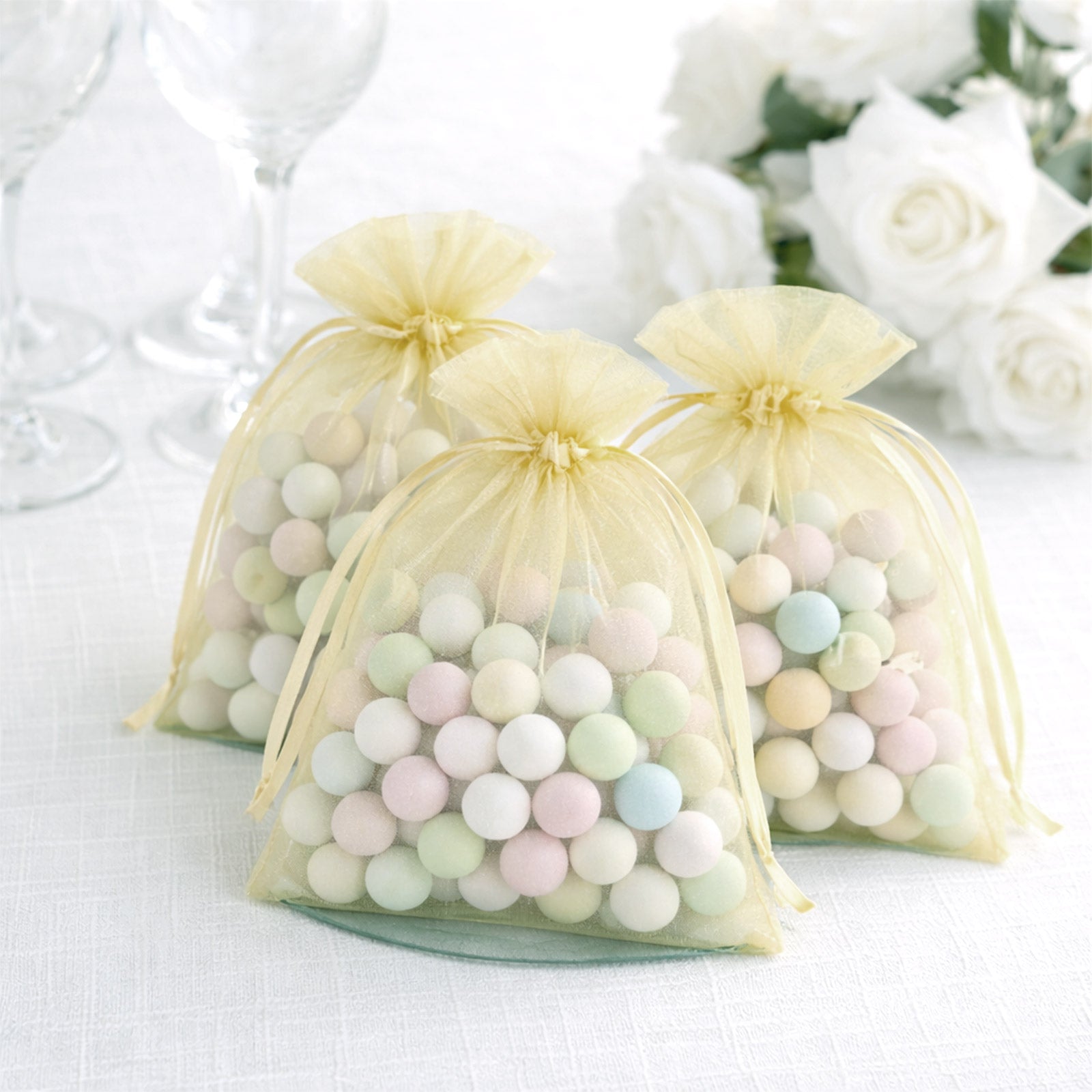 Yellow organza gift bags filled with pastel candies for party favors.