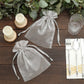 Silver organza gift bags on a wooden table with candles and utensils.