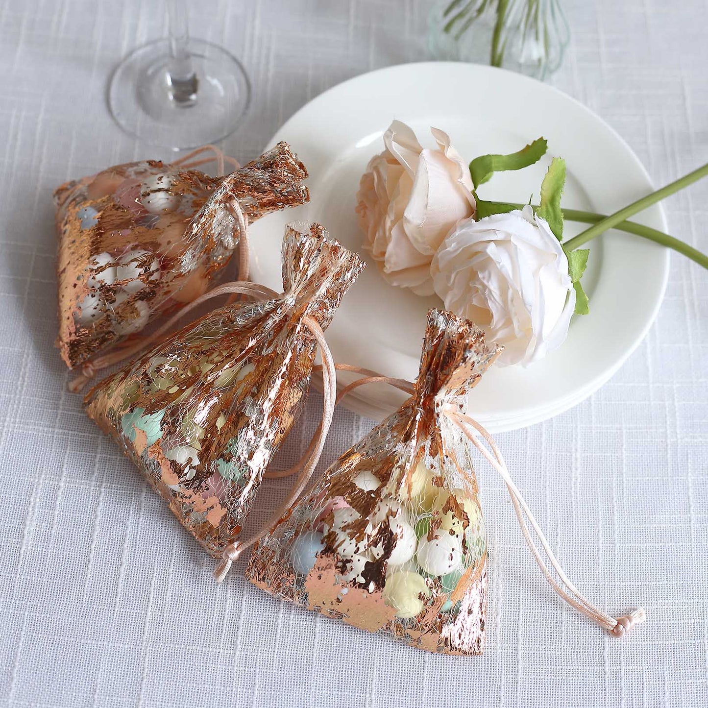 Metallic rose gold drawstring candy bags on a plate with flowers.